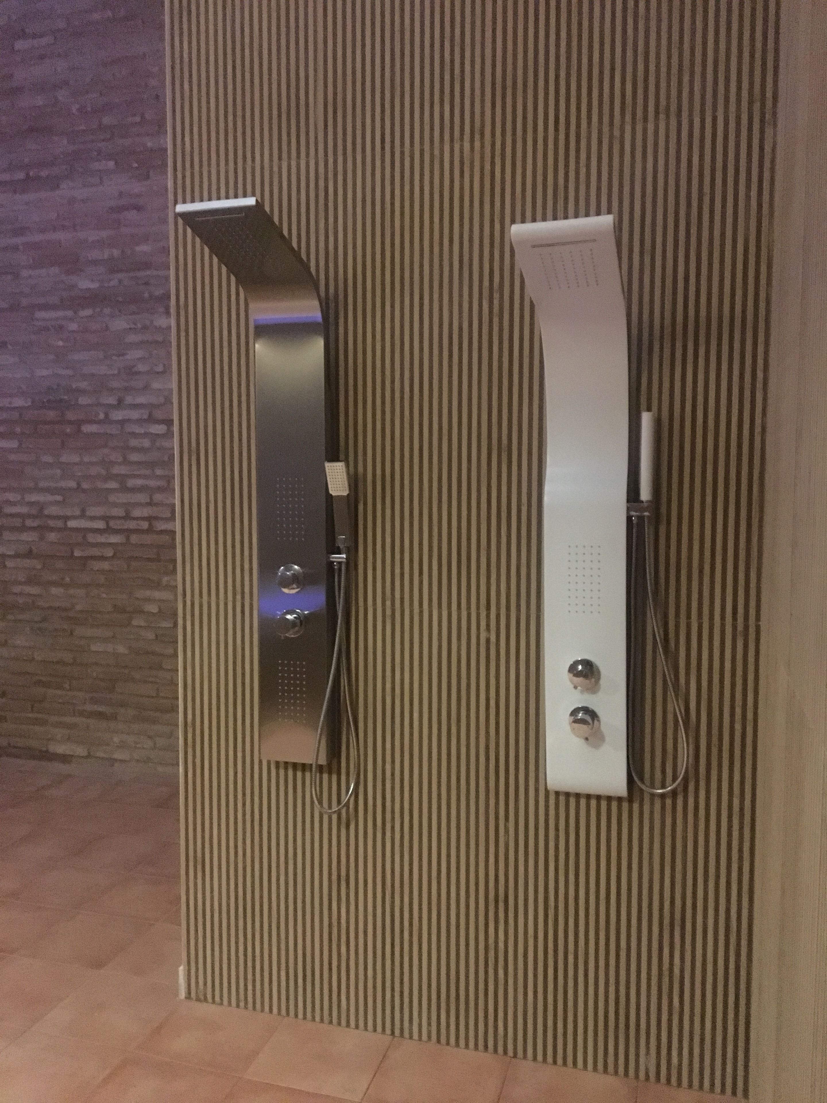 Een moderne badkamer met een gestreepte wand en een accentwand van baksteen. Er is een douche met een handdouche en een handbedienbare kraan.