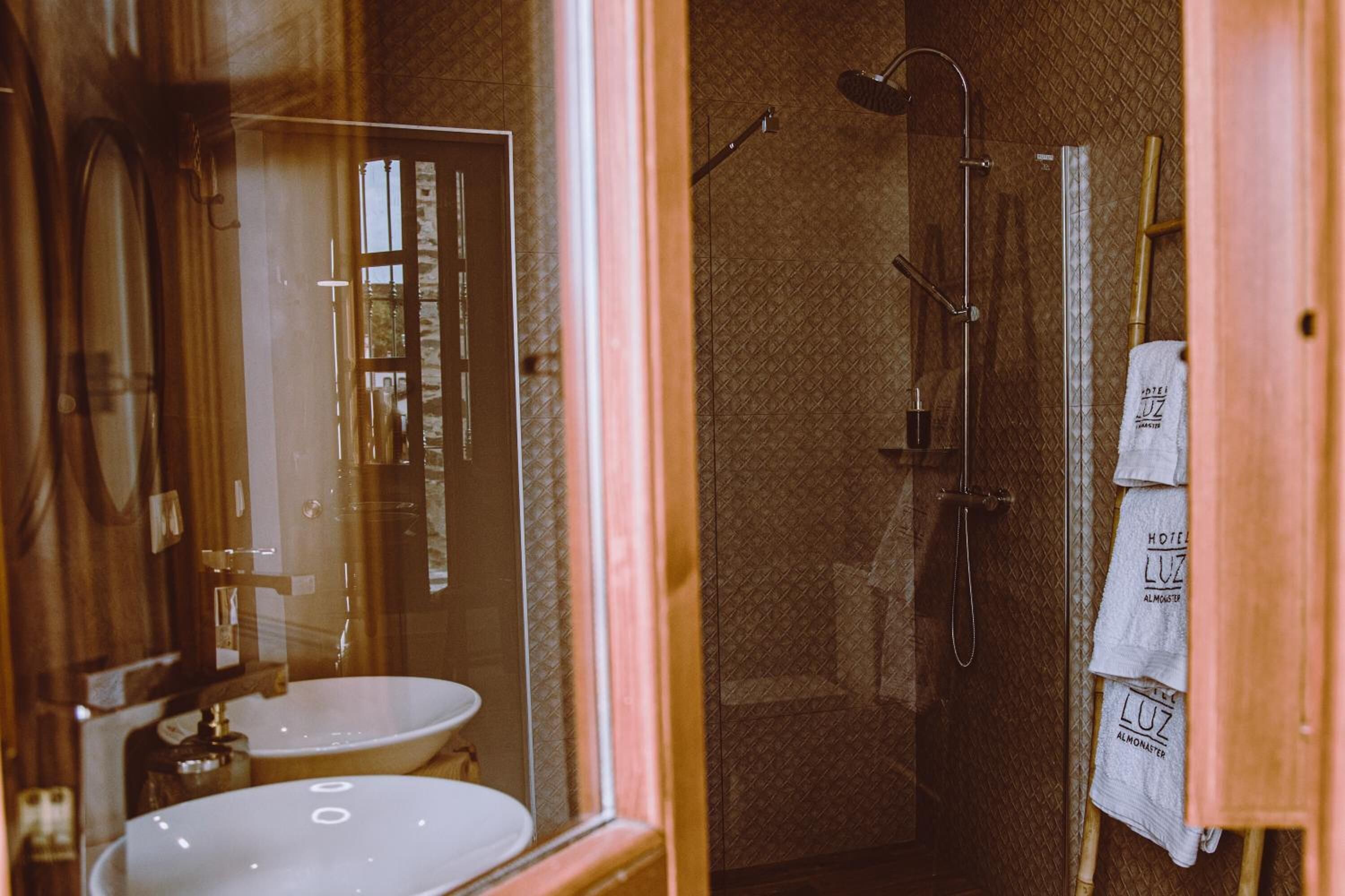 Un baño con lavabo, espejo, ducha y toallas colgadas en un perchero.