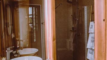 Un baño con lavabo, espejo, ducha y toallas colgadas en un perchero.
