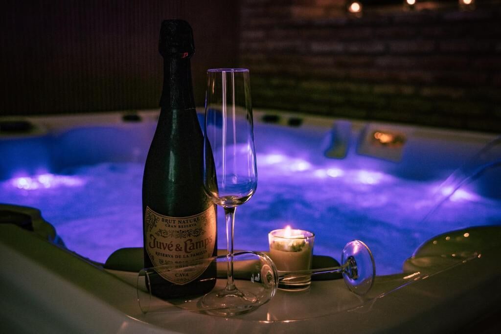 Une bouteille de vin Juvé & Camps et un verre posés sur une table dans un bain à remous, avec une bougie allumée.
