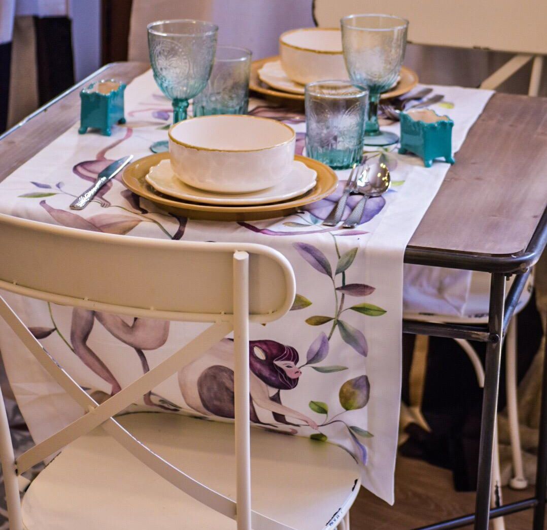 Een eettafel gedekt met borden, kommen en glazen, en een stoel met een tafelkleed met bloemen.