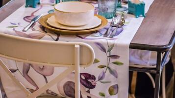 Een eettafel gedekt met borden, kommen en glazen, en een stoel met een tafelkleed met bloemen.