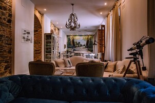 Una sala de estar acogedora con un sofá azul, una araña, un telescopio y un mural en la pared.