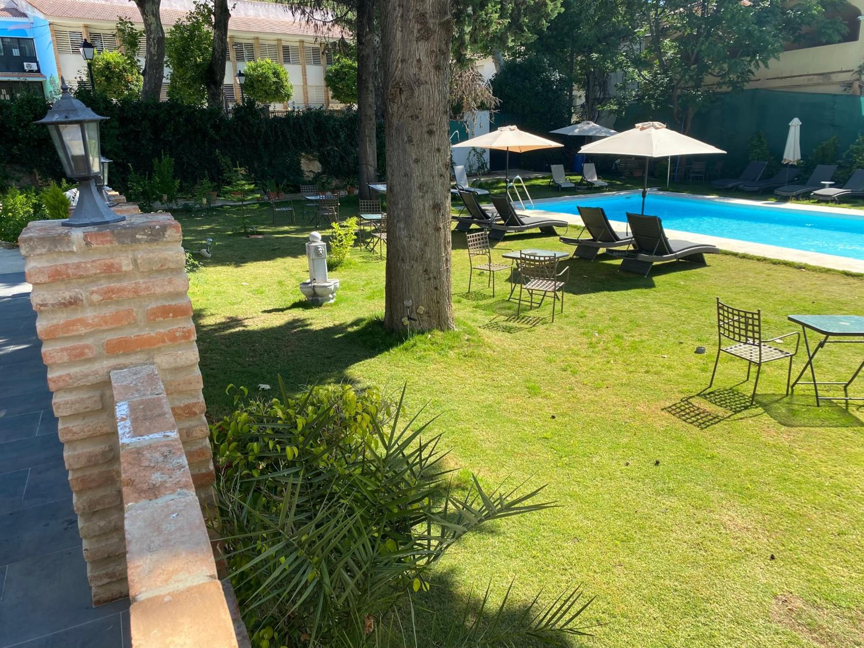 A well-maintained pool area with lounge chairs and umbrellas, surrounded by greenery and a brick wall.