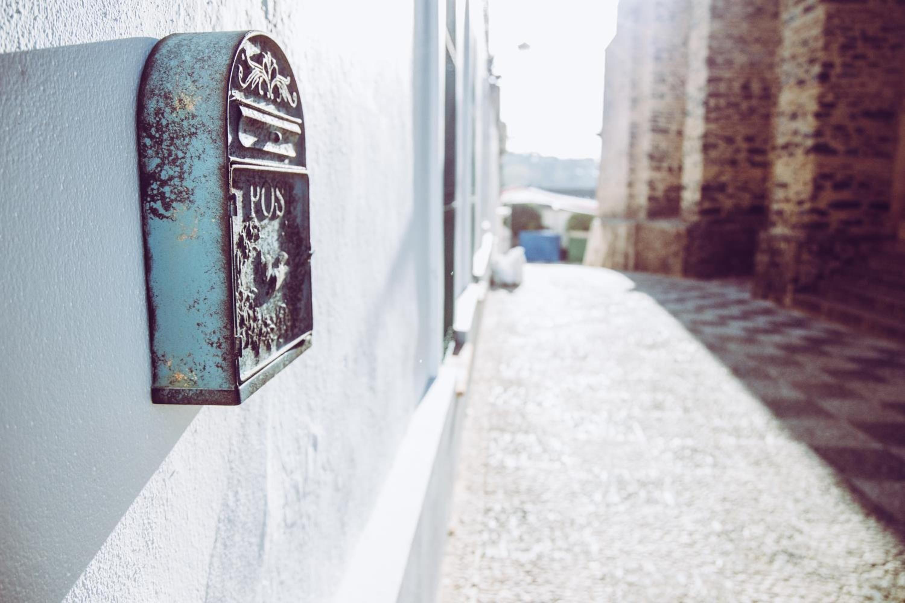 Une ruelle étroite avec une boîte aux lettres usée fixée à un mur blanc.