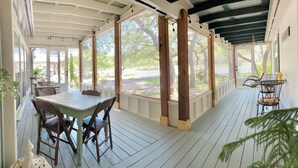 A covered porch with a table and chairs, large windows, and a view of the outdoors. - BellaVida B&B and Retreat (Wimberley)