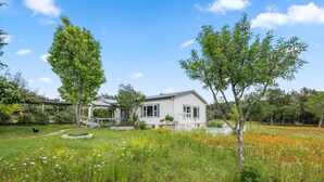 A house with a white exterior, surrounded by a lush garden with various flowers and trees. - BellaVida B&B and Retreat (Wimberley)