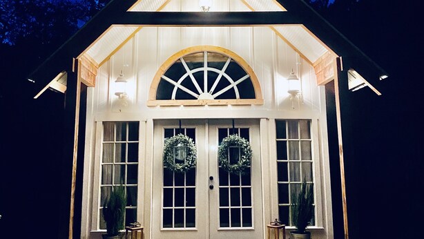 A small, illuminated building with a pitched roof, a large arched window, and two doors with wreaths. - BellaVida B&B and Retreat (Wimberley)