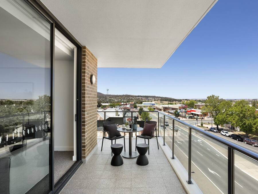 A balcony with a table and chairs, a view of a street, and a brick wall.