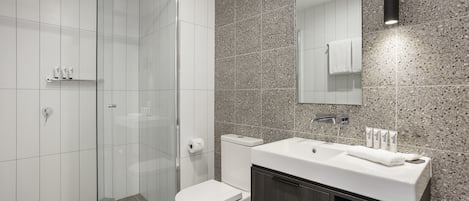 A modern bathroom with a glass shower enclosure, a white toilet, and a vanity with a mirror and sink.