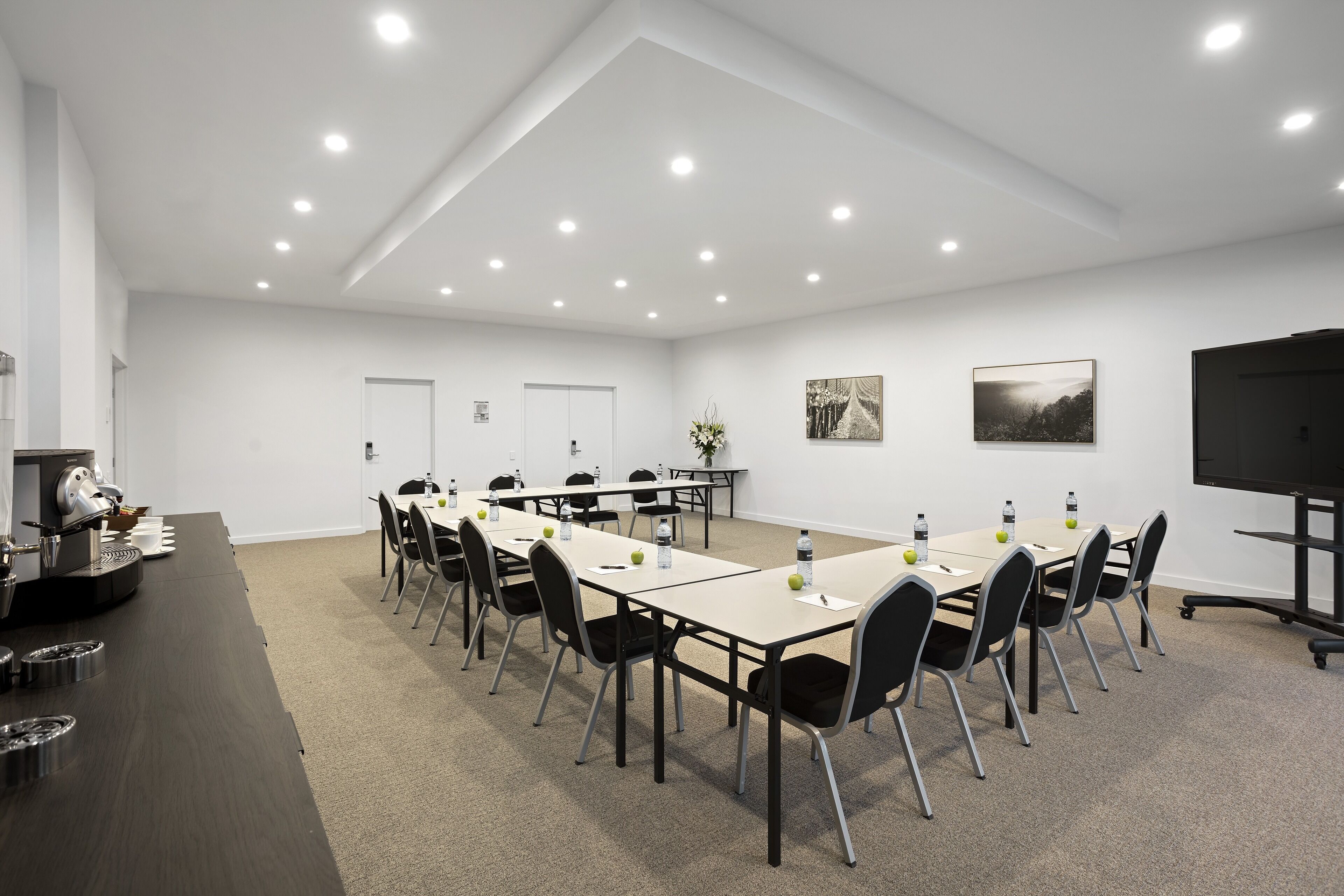 Une salle de conférence équipée d’une longue table, de chaises, d’un projecteur et d’une machine à café.