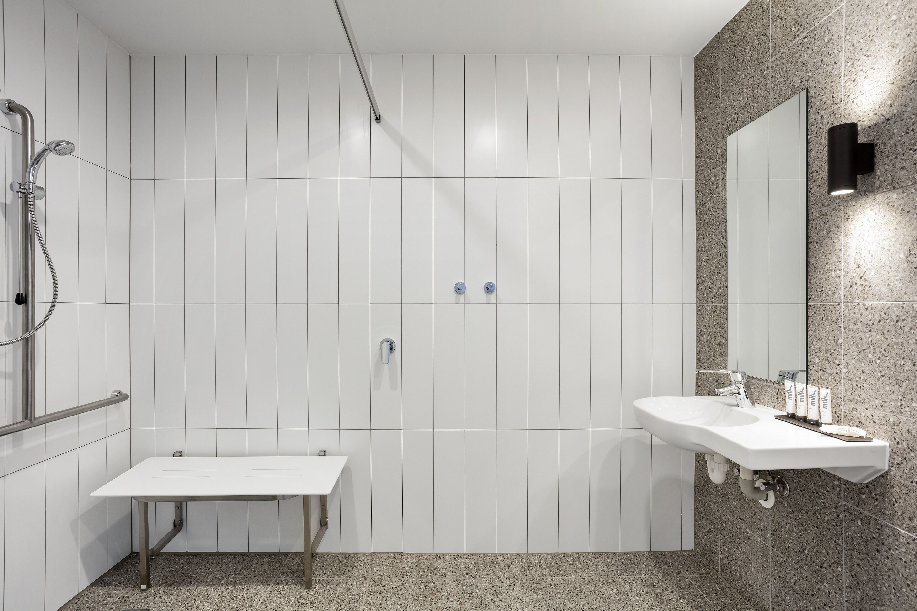 A modern bathroom with a white vanity, a shower with a handheld showerhead, and a wall-mounted mirror.