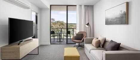 A modern living room with a flat-screen TV, a sofa, an ottoman, and a balcony with outdoor furniture.
