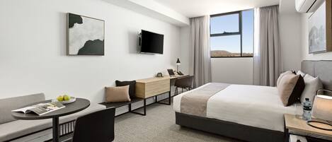 A modern hotel room with a bed, a desk, a sofa, and a TV.