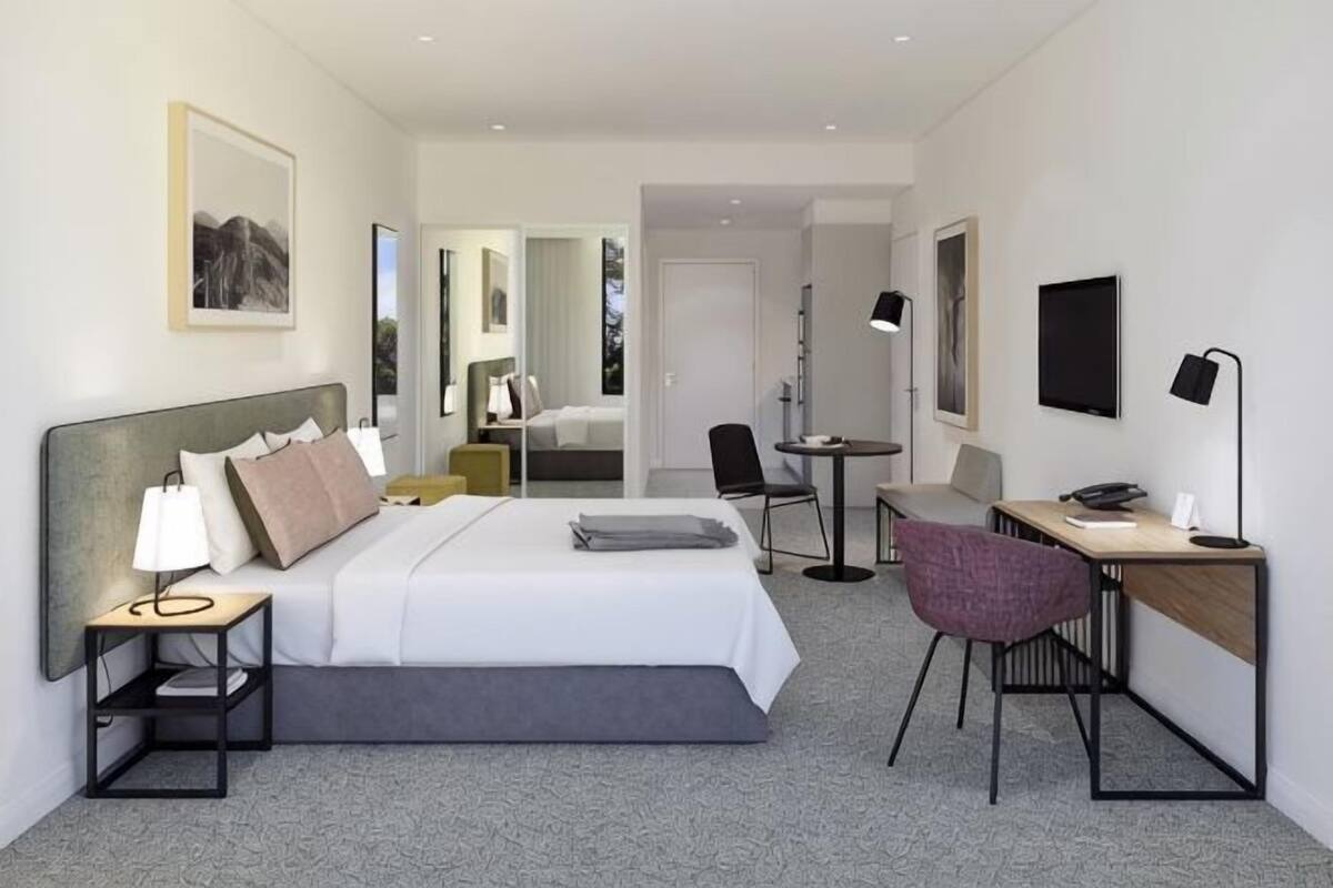 A modern hotel room with a bed, desk, chair, and a small table.
