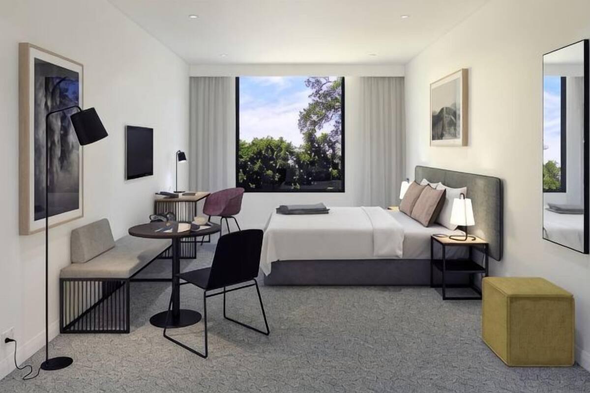A modern hotel room with a bed, desk, chair, and a view of the outdoors.