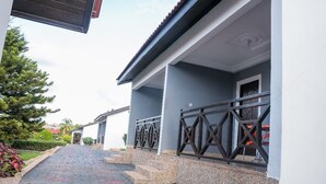 A building with a covered walkway leading to a door, surrounded by a low wall and a metal fence. - Rexmar Hotel (Kumasi)