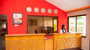 A reception area with a red wall, a clock, and a receptionist. - Rexmar Hotel (Kumasi)