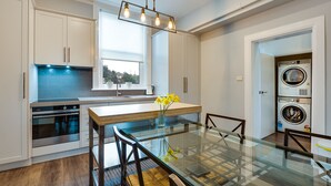Una cocina moderna con armarios blancos, una mesa de comedor de vidrio y lavadora secadora integradas.