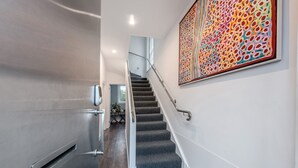 Una escalera moderna con barandilla de metal, un rellano alfombrado y un cuadro abstracto colorido en la pared.