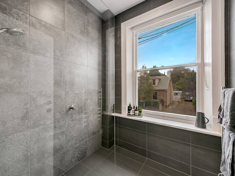 A bathroom with a shower, a window with a view, and a shelf with toiletries.