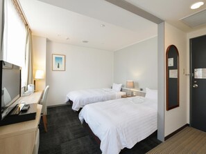 Two single beds, a desk with a flat-screen TV, and a comfortable seating area.