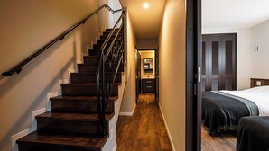 A wooden staircase with a handrail leading to a bedroom with a bed and a nightstand. - Tsukasa Condo Chatan Araha (Chatan)