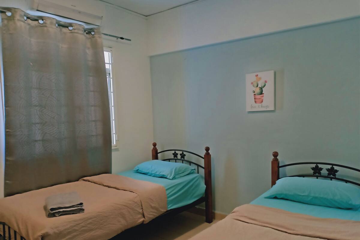 A bedroom with two single beds, a window with a curtain, and a wall-mounted picture.