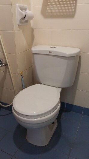 A white toilet with a tank labeled "American Standard" in a bathroom with beige tiles and a blue floor. - Couchbee at Perdana Exclusive Condominium (Petaling Jaya)