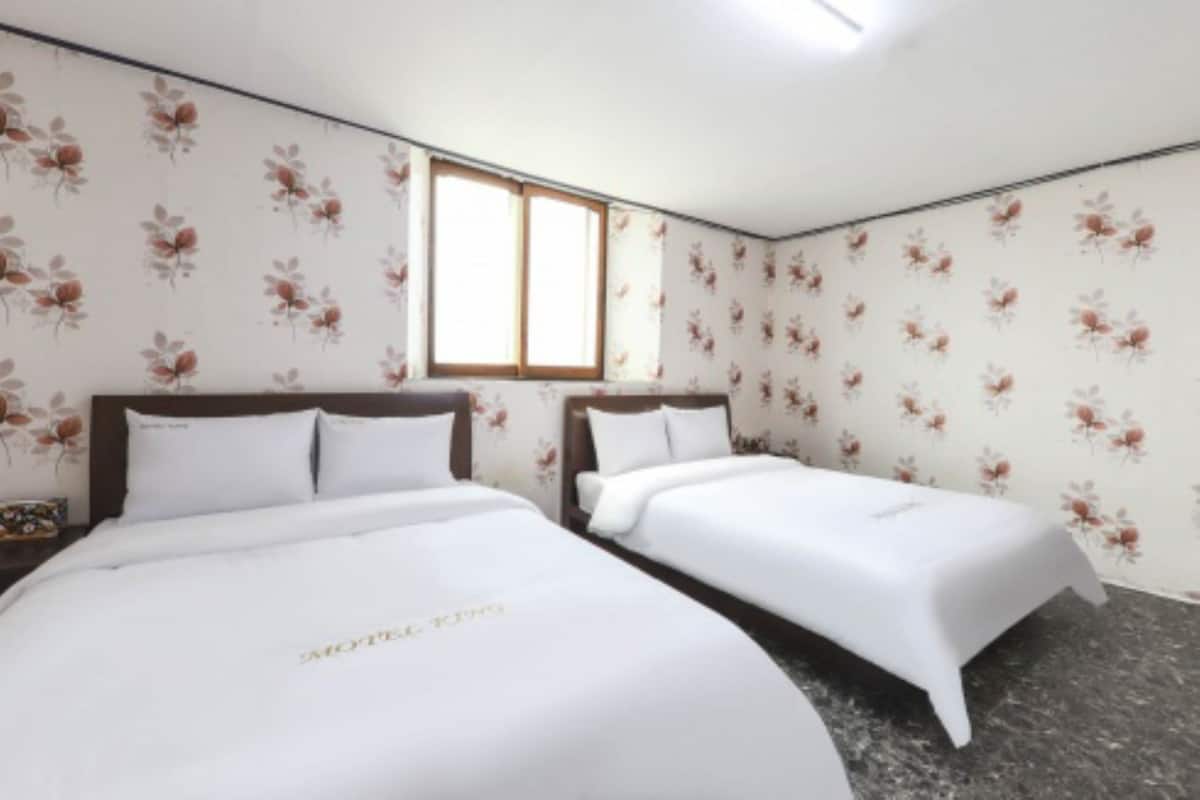 A hotel room with two single beds, floral wallpaper, a window, and a ceiling light.