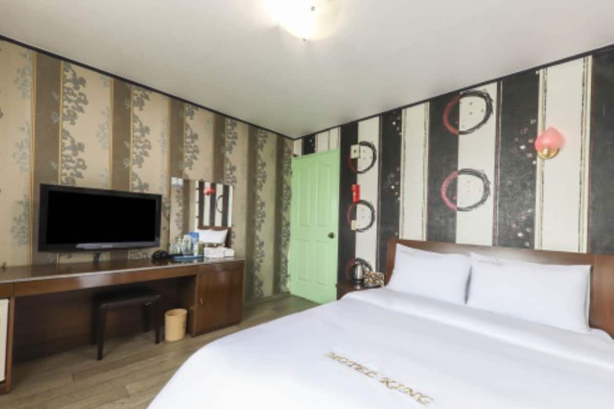 A hotel room with a bed, a desk, a television, and a green door.