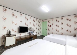 A hotel room with floral wallpaper, a television, a desk with a kettle, and two beds.