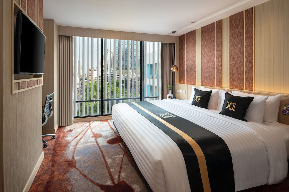 A hotel room with a large bed, a TV mounted on the wall, and a view of tall buildings through the window.