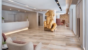 Een ruime lobby met een receptiebalie, een groot gouden sculptuur en moderne zithoeken.