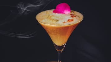 Una copa de martini con espuma arriba, sobre un posavasos de madera con un pétalo de rosa en el borde.