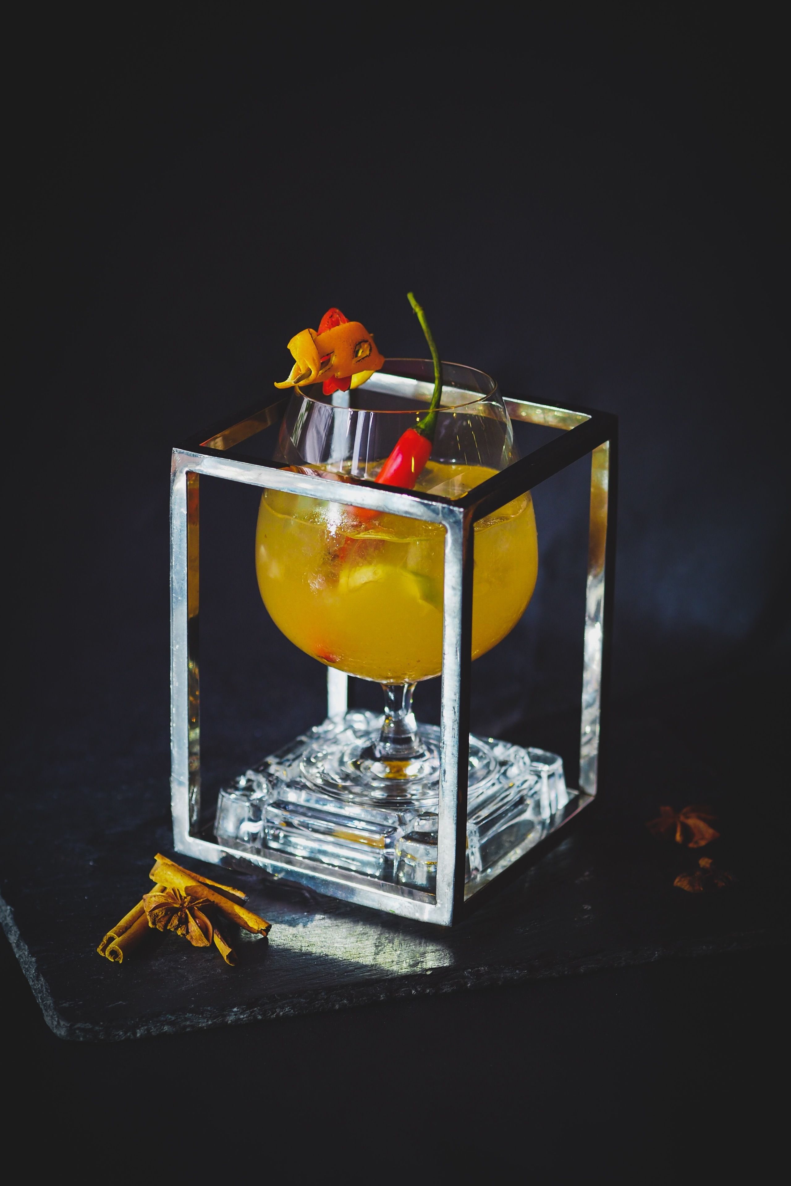 A cocktail in a glass with a square base, garnished with a flower and a chili pepper.