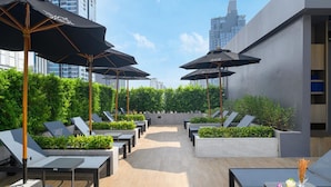 A rooftop lounge with sun loungers, umbrellas, and a view of the city skyline. - Eleven Bangkok Sukhumvit 11 by Kingston Hotels (Bangkok)