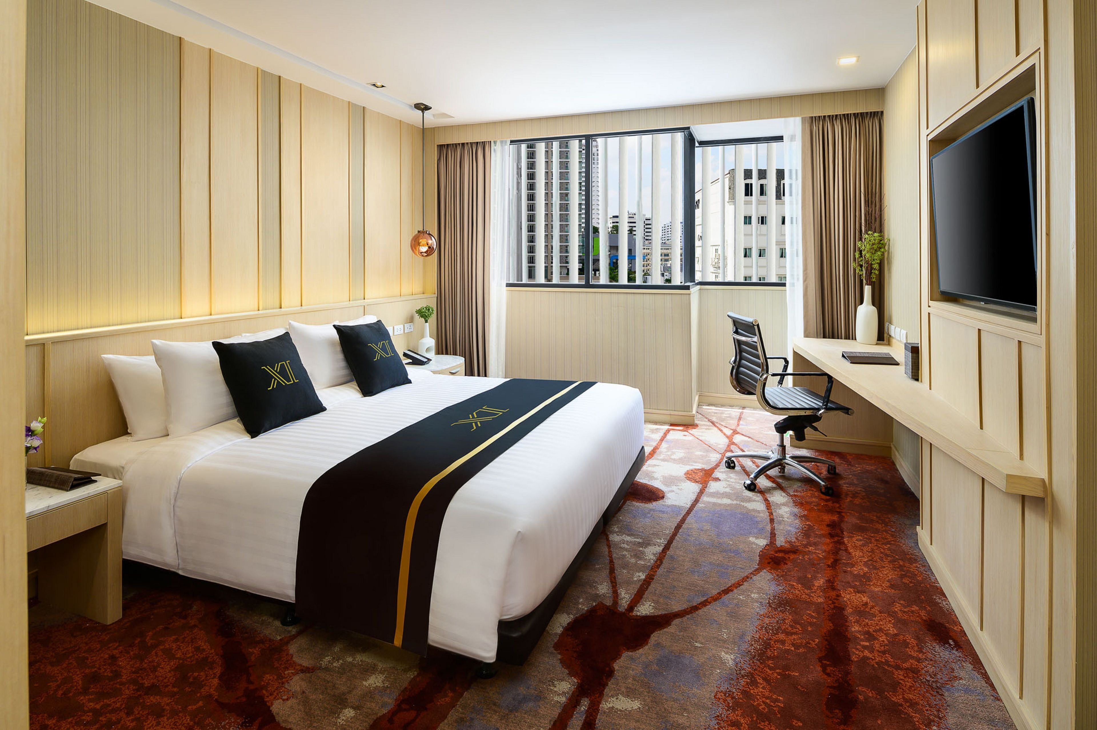 Une chambre d’hôtel avec un grand lit, un bureau avec une chaise, une télévision et une vue sur les immeubles par la fenêtre.