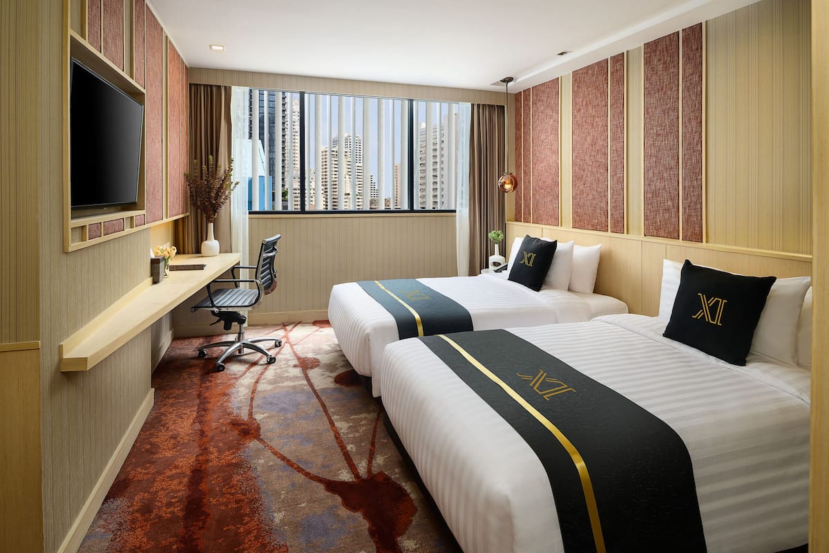 A hotel room with two beds, a desk, a TV, and a view of tall buildings.