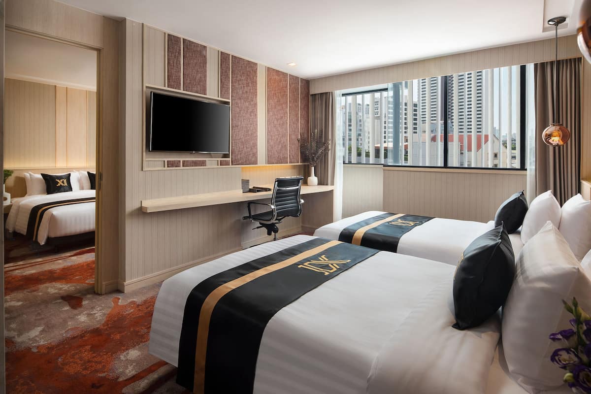 A hotel room with two beds, a TV, a desk, and a large window with a city view.