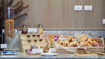 Un buffet de petit-déjeuner proposant diverses pâtisseries, une machine à café et un distributeur de jus de fruits.