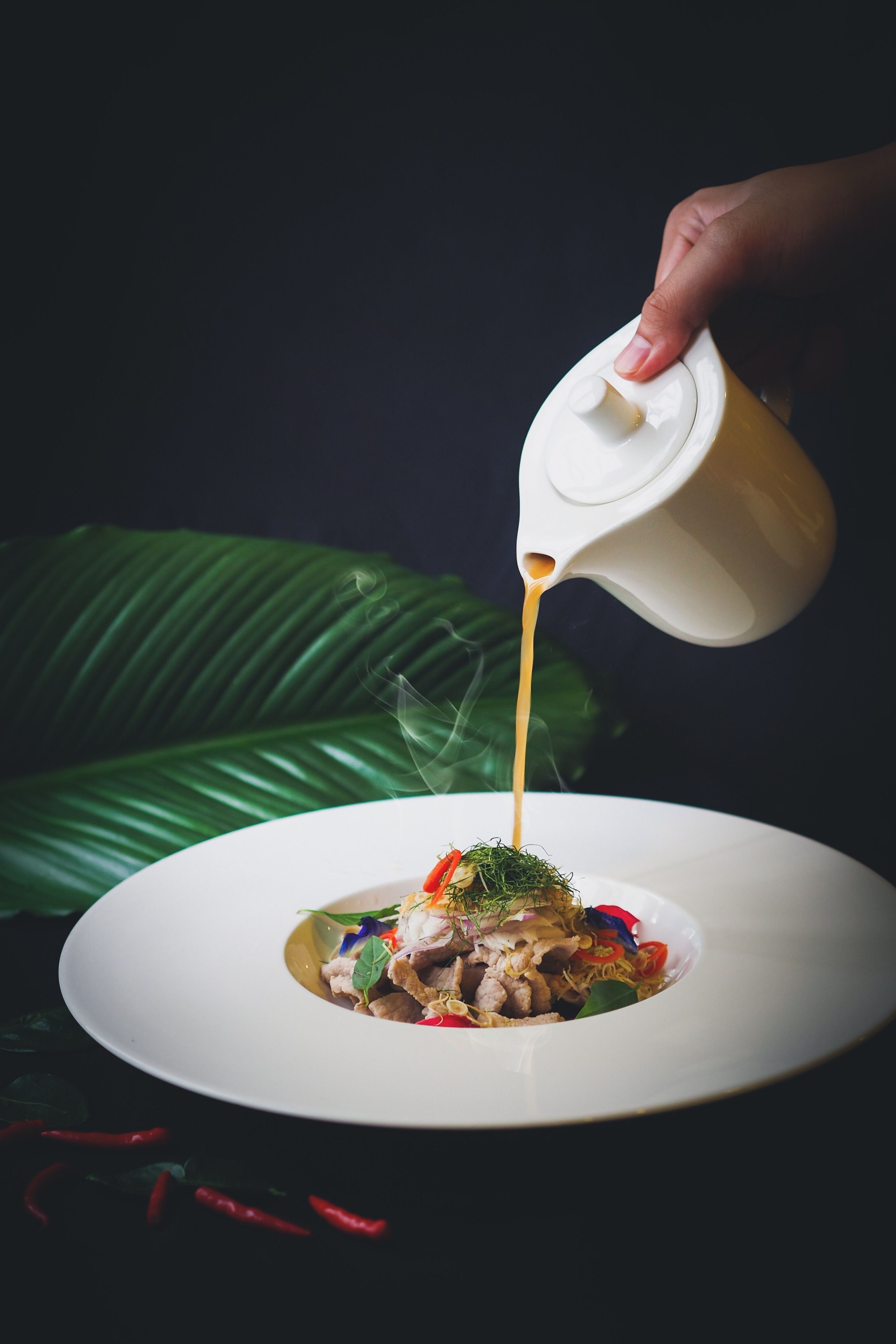 Una mano sirviendo salsa sobre un plato blanco.