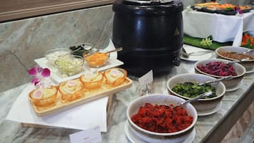 Un bufé con diversos alimentos, incluyendo una olla negra grande, tazones de verduras y una bandeja de pasteles.