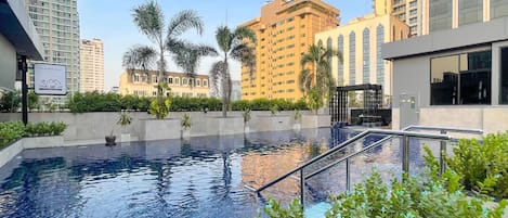 A swimming pool with a metal railing, surrounded by greenery and modern buildings in the background.