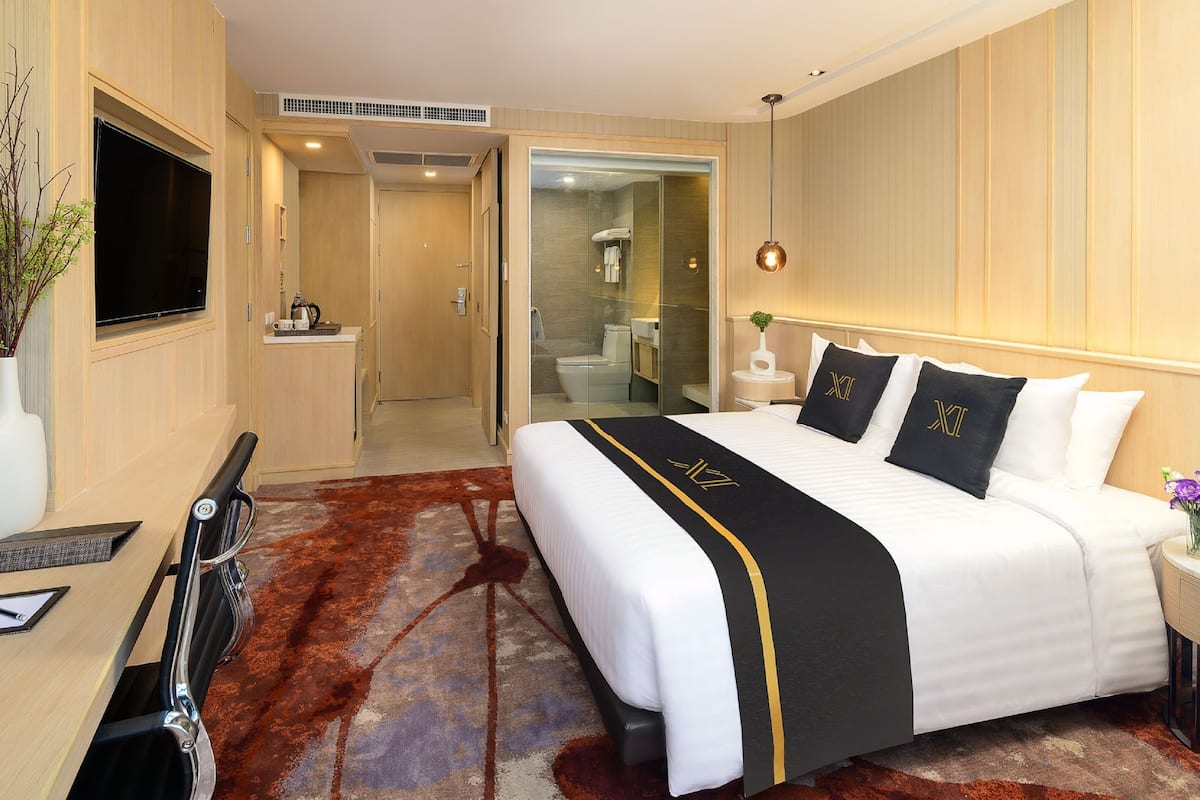 A hotel room with a large bed, a TV, a desk, and a bathroom visible through an open door.