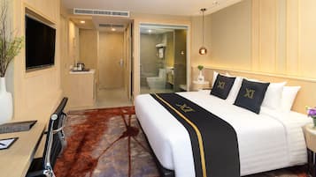 A hotel room with a large bed, a TV, a desk, and a bathroom visible through an open door.