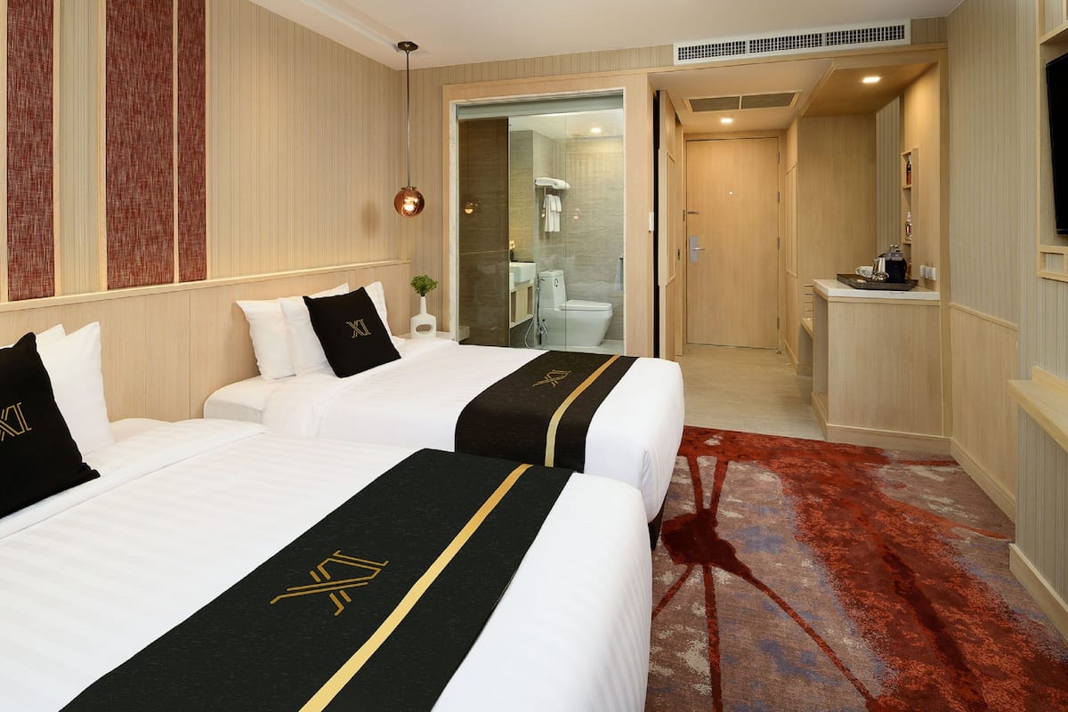 A hotel room with two beds, a red carpet, a bathroom, and a TV on the wall.