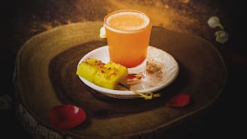 Un verre de jus d’orange sur une table en bois, avec une tranche d’ananas et un pétale de fleur.