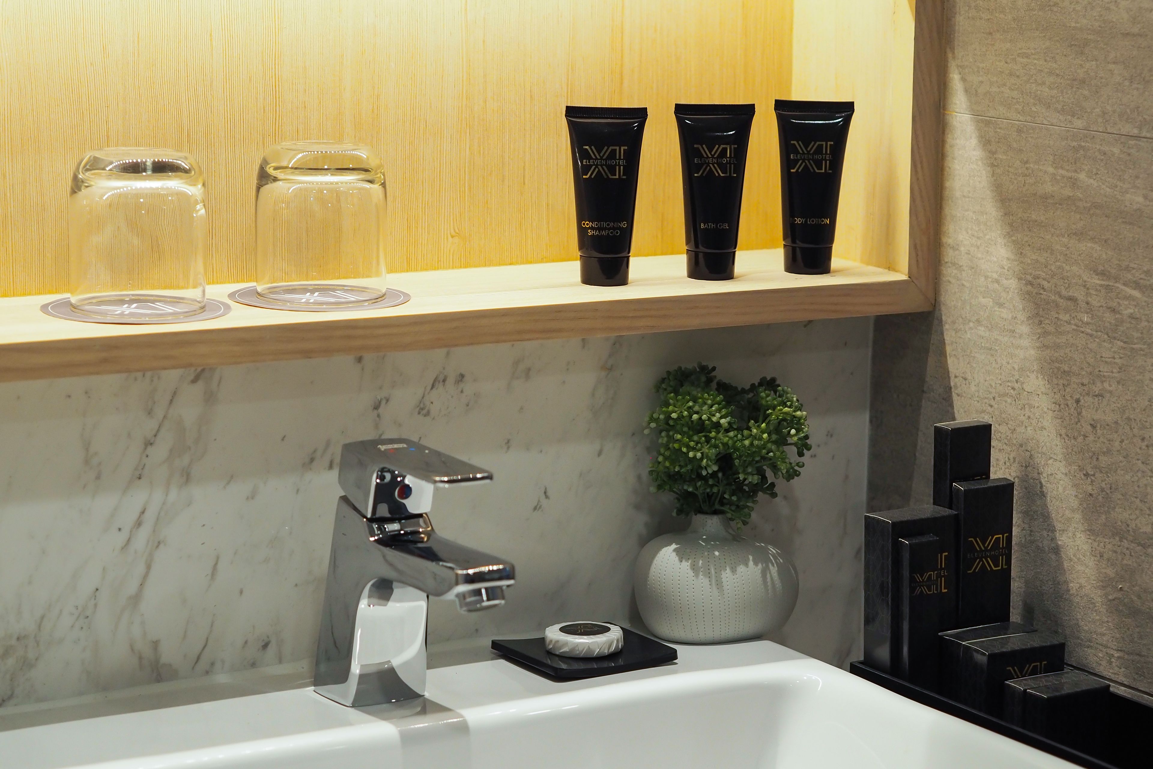 A bathroom with a marble sink, a modern faucet, and a shelf with toiletries.