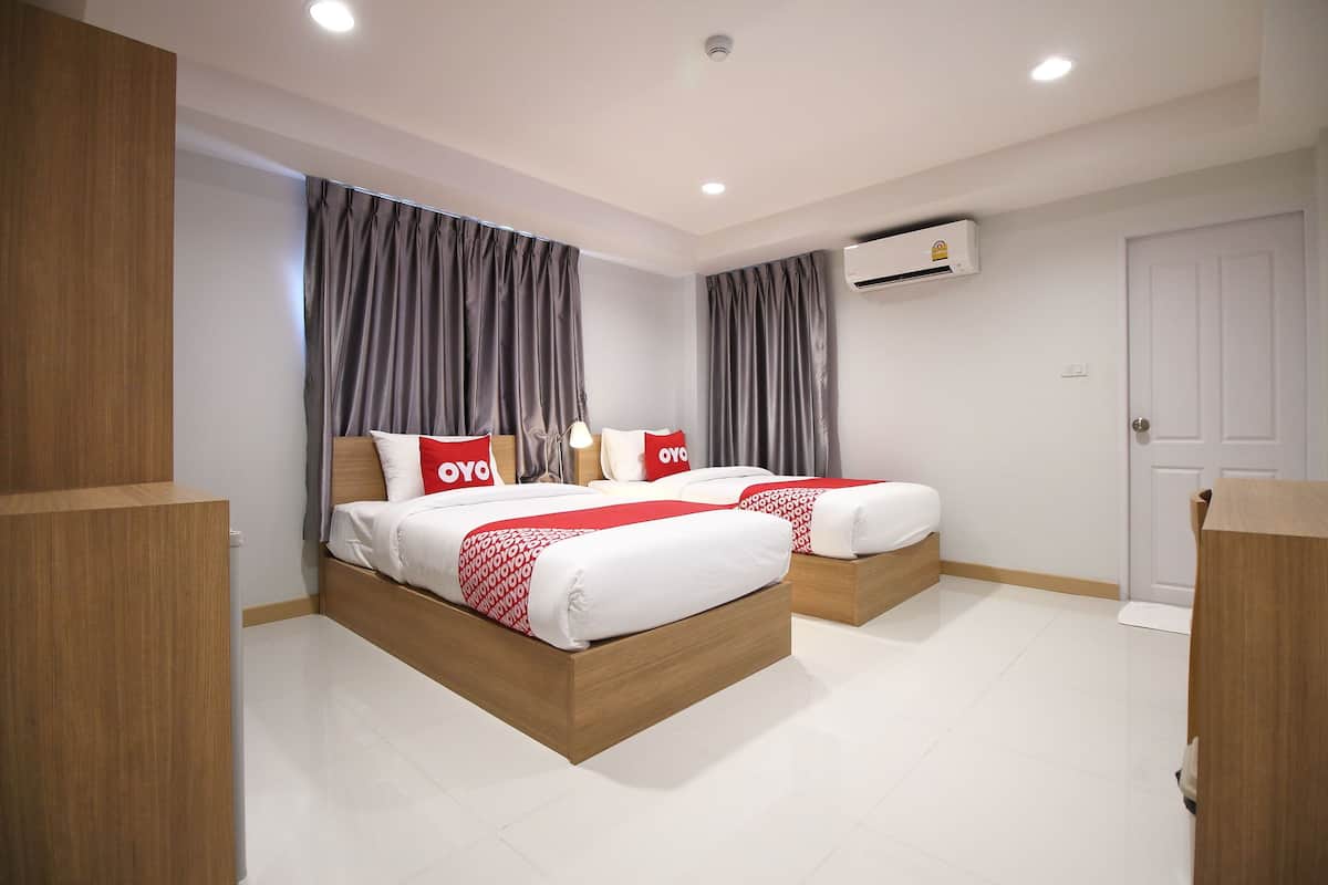 Une chambre d’hôtel moderne avec deux lits, des rideaux gris, un appareil de climatisation et une porte blanche.
